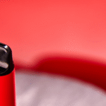 Close-up of a sleek red vape device with a black mouthpiece, set against a soft red background, highlighting its modern and stylish design