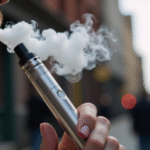 A man is vaping, surrounded by a casual atmosphere while exhaling vapor.