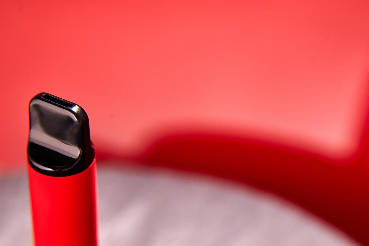 Close-up of a sleek red vape device with a black mouthpiece, set against a soft red background, highlighting its modern and stylish design