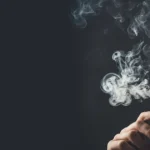 Man exhaling cigarette smoke in a dark setting.