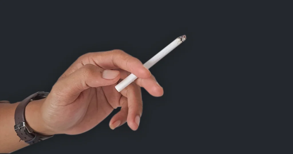 Hand holding a lit cigarette against dark background.