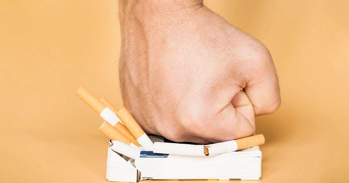 Hand crushing a pack of cigarettes, symbolizing quitting smoking.