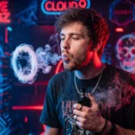 A man exhaling a thick ring of vape smoke in front of a neon-lit background sign.